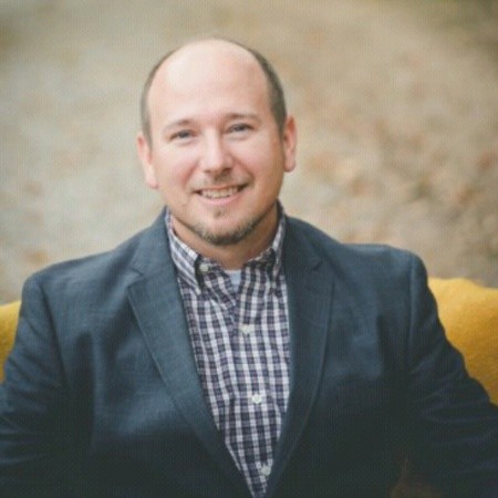 Nick Ware wearing a navy blue business jacket and blue and white plaid, collared shirt underneath.